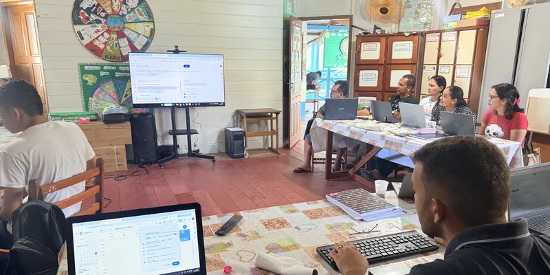 Educadoras y educadores de la Escola Ixubãy Rabuī Puyanawa trabajan con ordenadores portátiles frente a la pantalla de gran formato del aula multimedia