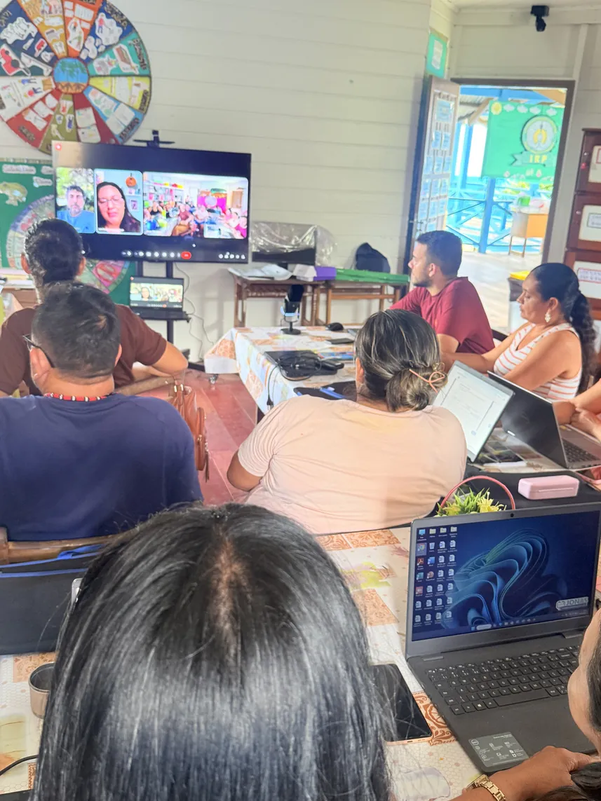Educadores indígenas siguen una clase por videoconferencia en una pantalla grande del aula