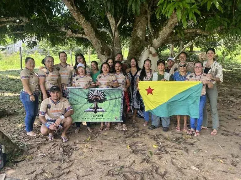 Miembros de la comunidad educativa nukini bajo un árbol, con la bandera del pueblo Nukini y la del estado de Acre
